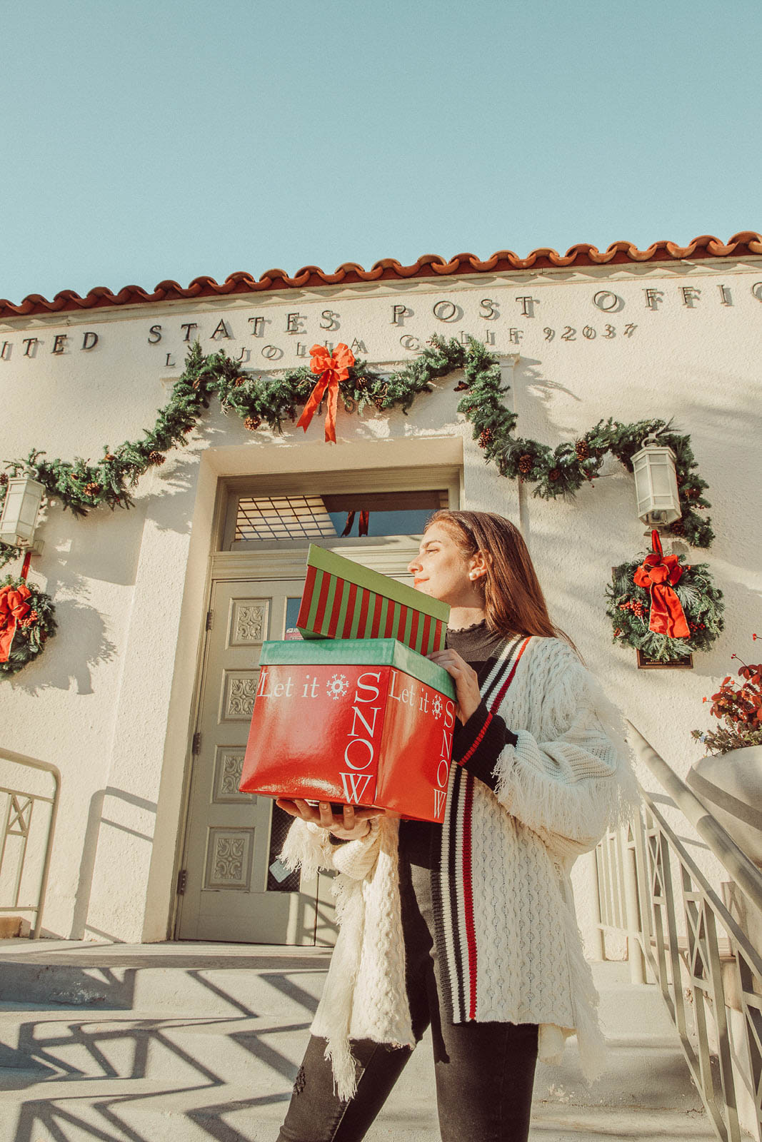 Woman wearing white sweater holding Christmas gifts in front of post office - 5 Creative Christmas Photoshoot Ideas to Try This Season