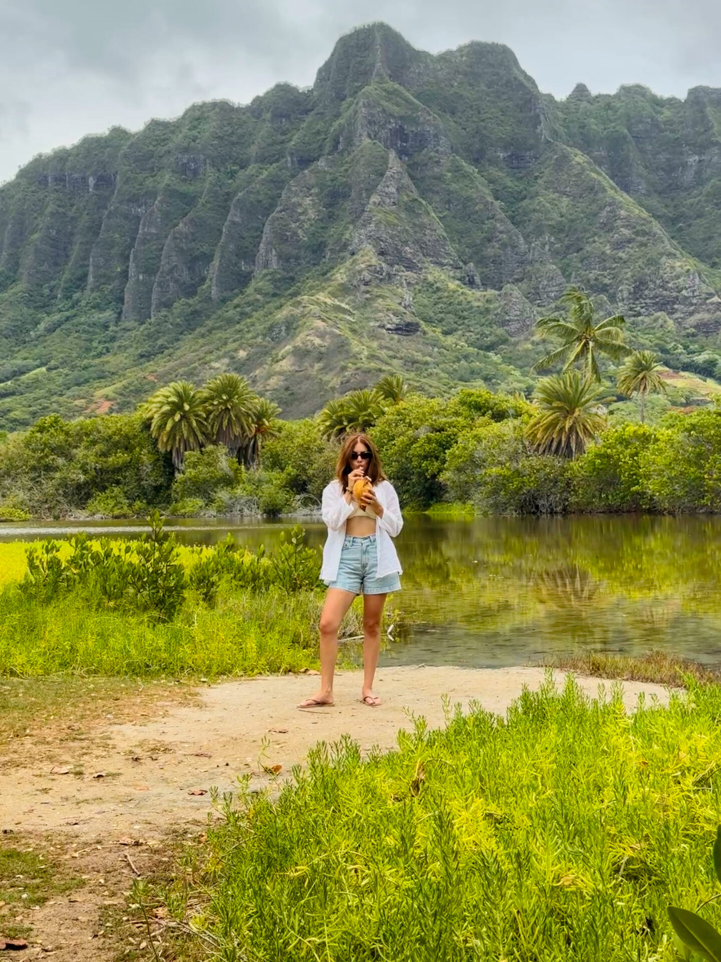 Me standing in front of the 'Apua Fishpond drinking from a coconut, with the Ko'olau Mountains in the background.